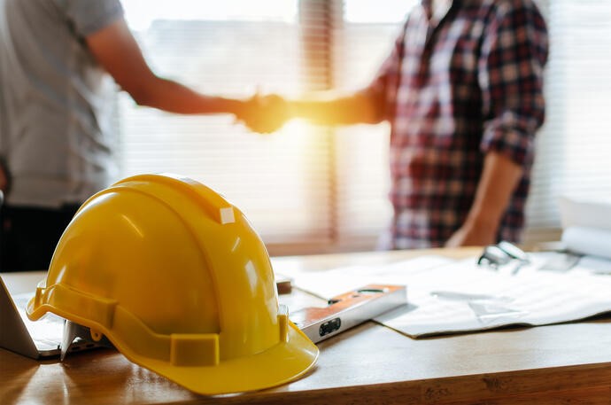 Man Shaking Hands Next To A Yellow Hard Hat On A Table